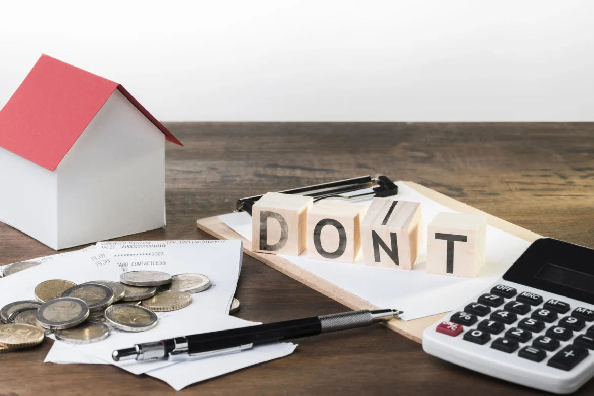 Wooden blocks spelling “DON’T” placed next to a small house model, calculator, coins, receipts, and documents, symbolizing financial mistakes or warnings related to home loans and property purchases.